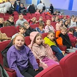 Uczniowie siedzą na krzesłach oczekując na spektakl.