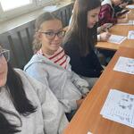 Uczennice pozują do zdjęcia. Uczniowie wykonują zadania na kartach pracy.
