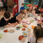 Ucznoiwie stoją dookoła prostokątnego stołu. Na stole na talerzach znajdują się składniki na pizzę.jpg