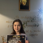 Uczennica pozuje do zdjęcia z dyplomem.