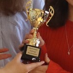 Zbliżenie na wręczanie złotego pucharu z tabliczką ‘Mistrzowie Dobrego Wychowania’, trzymanego przez grupę uczniów.