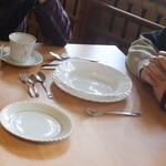 Stół nakryty zestawem naczyń i sztućców, z dwiema osobami siedzącymi po bokach.