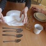 Uczniowie nakrywają do stołu, układając talerze, serwetki, szklanki i sztućce na drewnianym blacie.