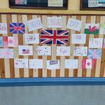 Gazetka ścienna z pracami uczniów przedstawiającymi flagi krajów anglojęzycznych i napisy „English” oraz „English Language Day”, wyeksponowana na korytarzu szkolnym.
