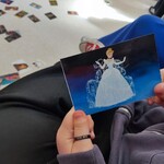 Uczennica trzyma kartę z ilustracją postaci z bajki, w tle na podłodze widoczne są inne karty.