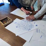 Uczniowie wykonują prace plastyczne przy stole – pocierają kredkami po kartkach, tworząc odbicia i faktury (m.in. wizerunek słonia), a obok leży pudełko z kolorowymi kredkami.
