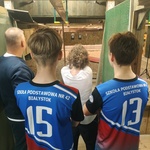 Uczniowie stoją na stanowisku strzeleckim i kierują uwagę na tarcze umieszczone w oddali.