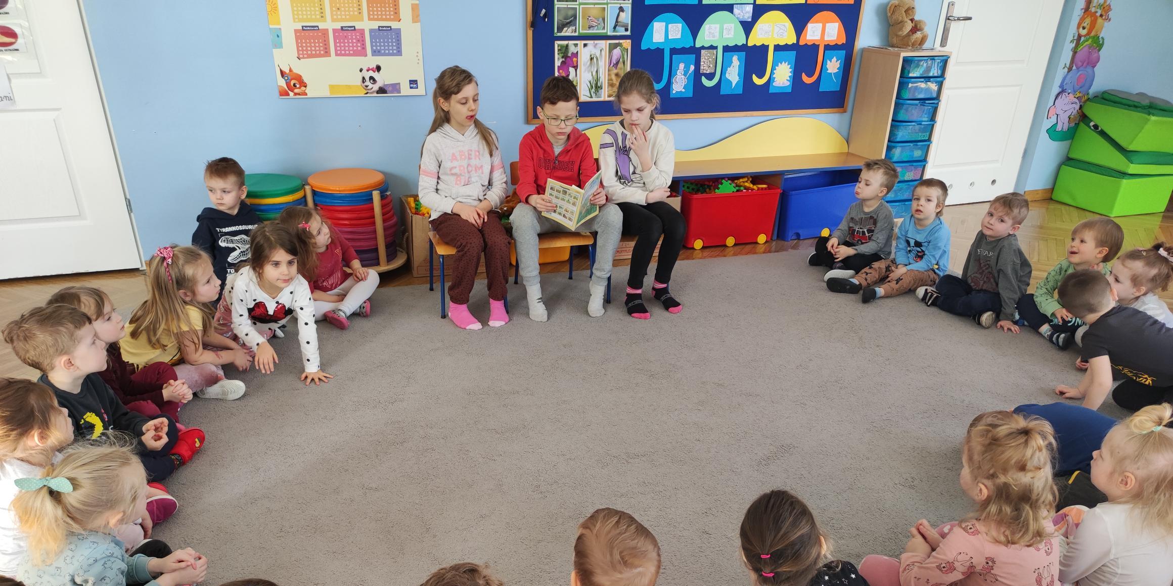 Uczniowie klasy 2c w przedszkolu czytają dzieciom książki